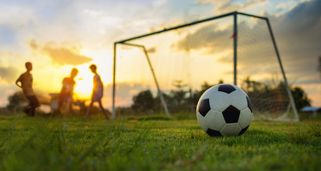 Soccer field with 3 kids, ball and net posts with a sunset background.